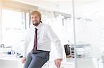 Portrait of smiling businessman wearing shirt and tie leaning on desk in office