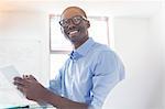 Portrait of young businessman wearing glasses and blue shirt holding digital tablet in office