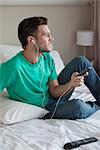 Young man sitting on bed listening to music with smartphone