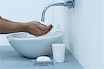 Man holding hands under dripping faucet in bathroom sink, cropped