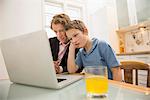 Bored father and son with laptop in kitchen