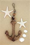 Starfish and cockle shells with decorative anchor on beach sand background.