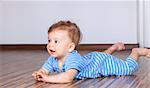 Portrait of a happy 6 months old baby boy crawling on wooden floor at home.