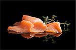 Smoked salmon pieces isolated on black background with fresh herbs. Culinary seafood.