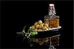 Olive oil in bottle and fresh olives in black bowl isolated on black background with fresh olive leaves. Luxurious culinary eating.
