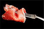 Delicious culinary prosciutto ham on silver fork isolated on black background. Culinary appetizer eating.