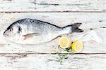 Delicious sea bream with lemon and fresh herbs on white textured wooden background, top view. Mediterranean seafood background.