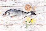 Delicious fresh sea bream fish with sea salt, herbs and lemon on white wooden textured background. Mediterranean seafood background in marine white. Culinary eating.