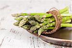 Fresh asparagus bundle on brown plate on white wooden textured background. Culinary healthy vegetable eating.