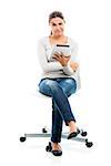 Beautiful female student sitting on a chair with a tablet, isolated over a white background