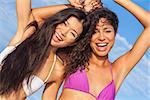 Two beautiful young women or girls, Asian and Latina Hispanic, in bikinis dancing on vacation on a hot sunny beach