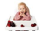 Portrait of sweet baby sitting on chair and eating plums.