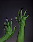 Green witch hands with black nails stretching up, Halloween theme, studio shot on black background