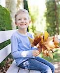 positive smiling boy enjoying autumn time with bouquet of golden tree leaves