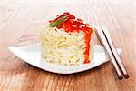 Delicious asian culinary eating. Rice with red vegetable sauce and chopsticks on wooden background. Minimal, sparse style.