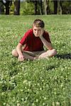 Depressed young Caucasian teen sitting on grass