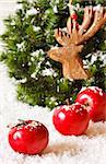 Christmas decoration with wreath, decorative wooden deer and fresh ripe red aplles on snow.