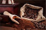 Traditional coffee still life. Ground coffee, coffee beans, coffee grinder, wooden spoon with coffee and bag with coffee beans on dark wooden background. Culinary aromatic coffee drinking.