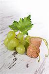 Green wine grapes with champagne cork on white wooden textured background. Vintage luxurious wine drinking.
