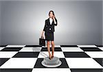 Beautiful businesswoman holding briefcase and using phone. Floor with checkerboard texture and gray wall