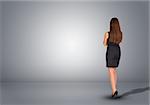 Businesswoman in dress standing in an empty gray room. Rear view. Hands crossed on his chest