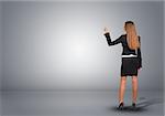 Businesswoman in suit standing in an empty gray room and pointing finger at wall. Rear view