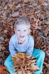 smiling little boy sitting in autumn leaves and holding a bouquet