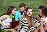 Cute teen with friends sitting outdoors on lawn