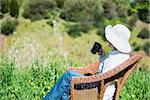 Woman  in profile sitting  on a wicker bench in the garden,holding a  cup of coffee and looking away