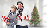 Festive mature couple holding christmas gifts against blurry christmas tree in room