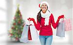 Festive brunette holding shopping bags against blurry christmas tree in room