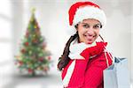Festive brunette holding shopping bag against blurry christmas tree in room