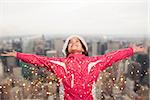 Cute girl in winter clothes with arms out against city skyline