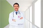 Handsome young doctor with arms crossed against modern white and green room with window