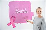 Happy young woman painting her wall pink against pink breast cancer awareness ribbon
