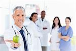 Mature doctor holding an apple wearing breast cancer awareness ribbon