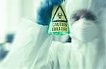 Scientist in protective suit holding beaker with caution sticker