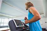 Side view of a young man running on treadmill in the gym