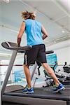 Rear view of a young man running on treadmill in the gym