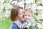 young mother and her little son hugging together in blooming trees at spring time