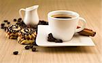 Cup of coffee with beans and cinnamon sticks over wooden background