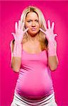 Pregnant attractive woman wearing rubber gloves posing over pink background