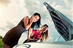 Two young women with broken car on a road