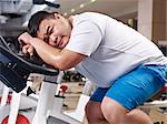 an overweight young man exhausted with exercising in fitness center.