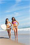 Beautiful young women surfer girls in bikinis with surfboards on a beach