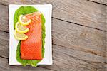 Fresh salmon fish with lemon and salad leaves on wooden table with copy space