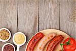 Various grilled sausages with condiments and tomatoes on cutting board with copy space