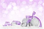 Christmas baubles and purple ribbon over snow bokeh background with copy space