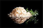 Natural sea salt heap isolated on black background with fresh herb thyme. Luxurious sea salt.