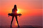 Beautiful and fashion young woman posing at teh sunset with a skateboard